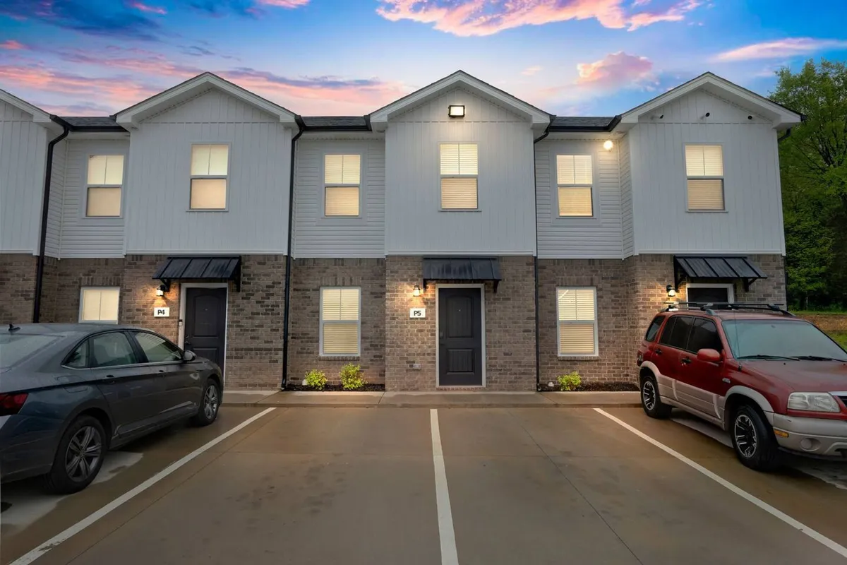 A welcoming view of the townhouse facade showcases the front doors, well-maintained landscaping, and ample parking spaces. The setting suggests a friendly, approachable neighborhood ideal for both short and long-term stays.