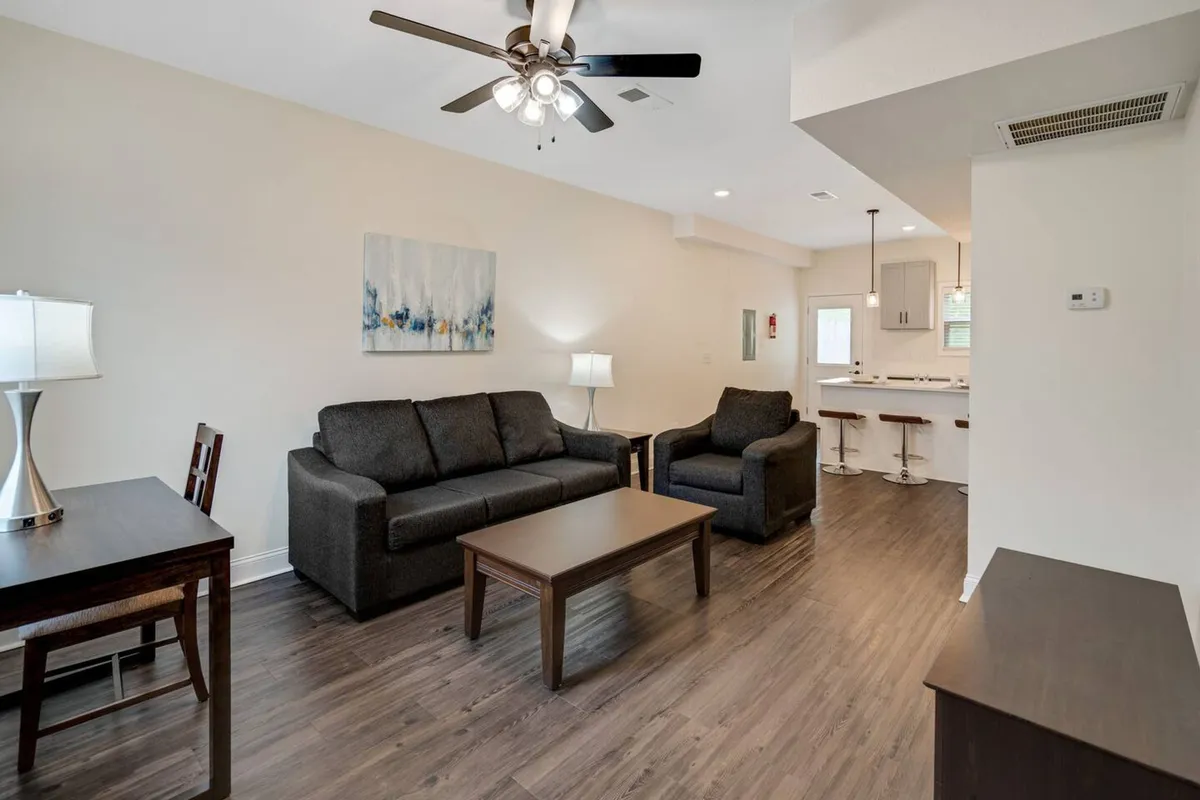 A luminous, open-concept living and dining area featuring a plush sofa, stylish coffee table, curated artwork, a contemporary lamp, and a dining table set in the background. The furnishings and décor exude elegance and comfort, with tasteful accents that create a sophisticated and inviting atmosphere.