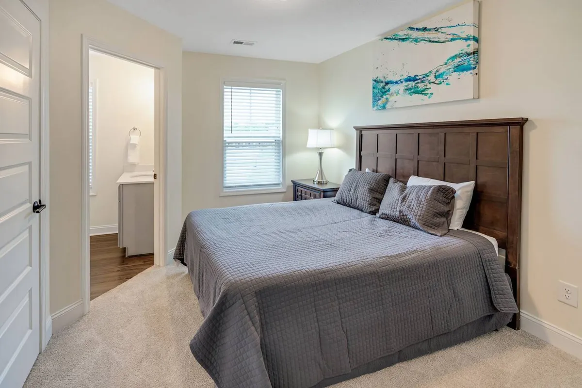A bedroom with a neatly made bed, nightstand, artwork above the headboard, and a softly glowing lamp. The space exudes warmth and tranquility, ideal for unwinding after a long day.