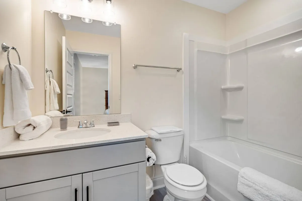 A modern ensuite bathroom with a vanity and sink, large mirror, bathtub, and toilet. The space is bright, clean, and inviting—ideal for both rejuvenating soaks and morning routines.