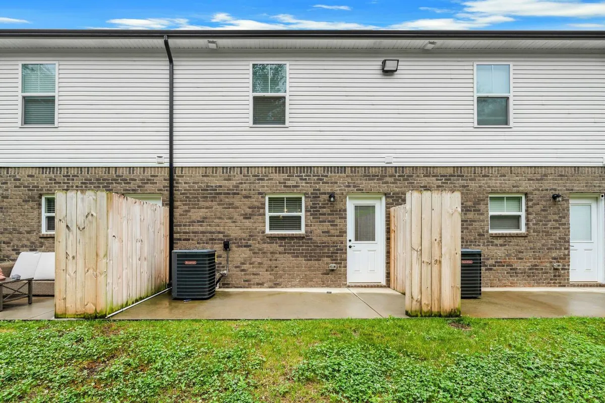 An inviting brick facade features a private fenced yard and a cozy patio area, perfect for outdoor relaxation or casual meetings. The scene is bathed in natural light, conveying a sense of comfort and tranquility.