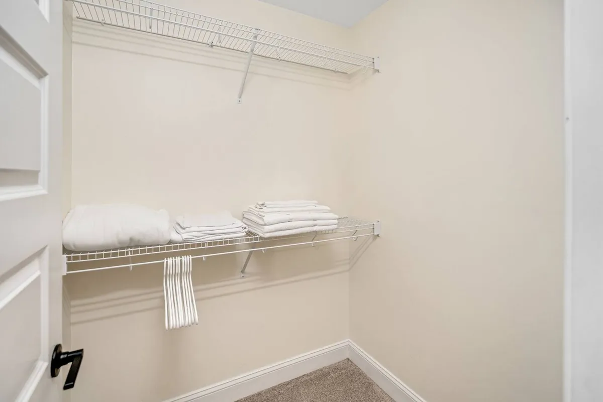 Shelves neatly stocked with fresh towels are set against clean walls and soft carpeting, conveying a sense of organization and readiness. The space is practical, with essentials clearly provided for immediate use.